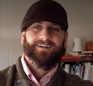 A headshot depicts a beareded and smiling Tim wearing a brown hat