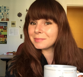 A headshot depicts Les sitting before a well posted wall holding a robust cup of coffee.